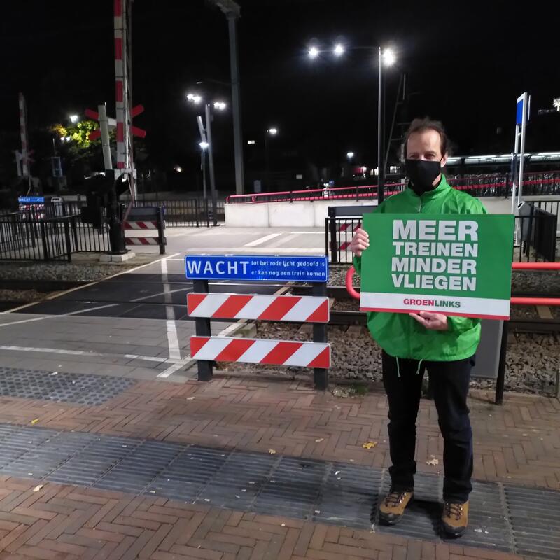 Michel met een protestbord "meer treinen minder vliegen" op station Wijchen, in de avond.