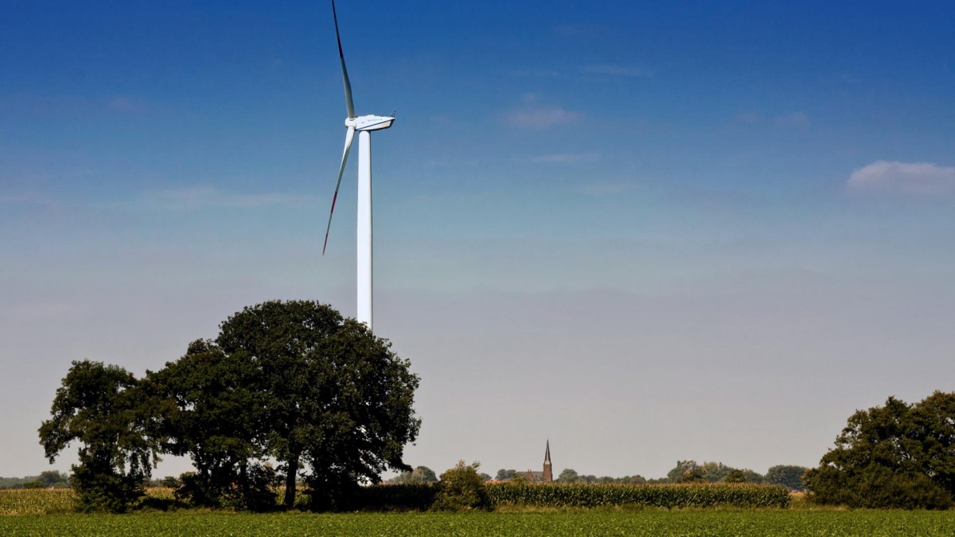 Een windmolen in een weide, met een kerk op de achtergrond.