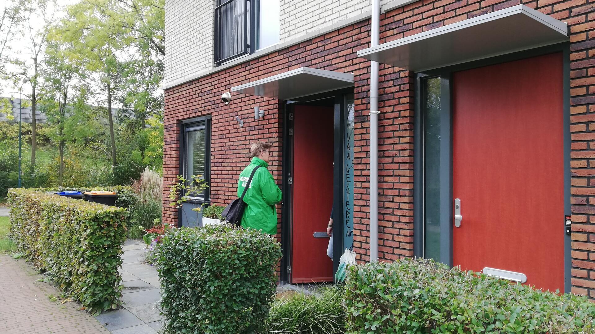 Een GroenLinkser staat aan de deur van een woning en is in gesprek met de bewoner.